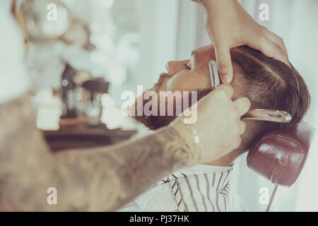 Hombre con una barba con una navaja de afeitar en una barbería. Foto en estilo vintage Foto de stock