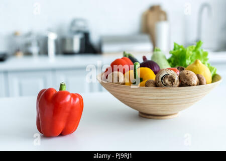 Vista cercana de pimiento y recipiente con hortalizas frescas en la mesa de la cocina