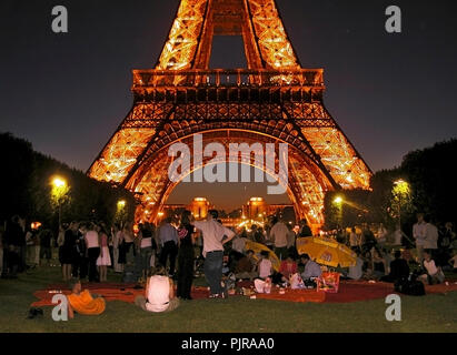 Torre Eiffel iluminada por la noche, con una fiesta en el Champ de Mars en primer plano: París, Francia Foto de stock