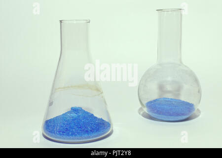 El material de vidrio de laboratorio con polvo cristalino de color azul brillante sustancia. Matraz Erlenmeyer delante del matraz, de forma redonda, antecedentes de tonalidad verde. Foto de stock
