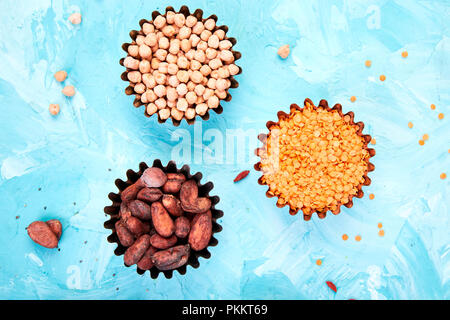 Diversas fuentes alimenticias en un tazón pequeño, sobre fondo azul. Súper alimento como materia de cacao, garbanzos, lentejas. Copie el espacio. Sentar planas. Foto de stock