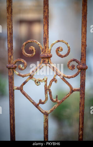 Antigua puerta de hierro oxidado con la letra K, casa abandonada en segundo plano. Foto de stock