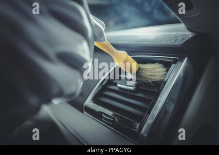 Limpieza del interior del coche con cepillo, servicio de detalles del coche.  Joven agradable hombre negro haciendo el interior del coche y la limpieza  del asiento con cepillo especial Fotografía de stock 