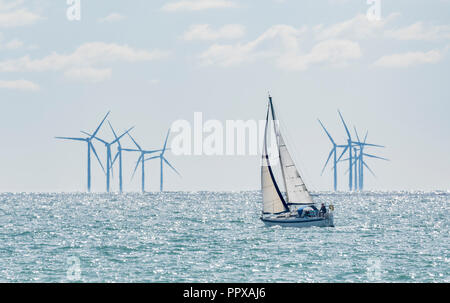 Yate de vela en el mar en frente de los aerogeneradores del parque eólico offshore Rampion fuera de la costa sur de Inglaterra, Reino Unido.