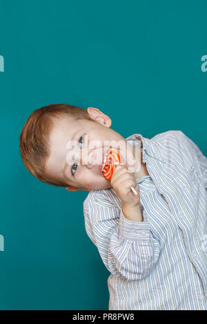 Niño lindo comiendo un lollipop sobre fondo verde. Niño boy comiendo piruleta aislado Foto de stock