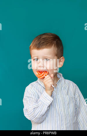 Niño lindo comiendo un lollipop sobre fondo verde. Niño boy comiendo piruleta aislado Foto de stock