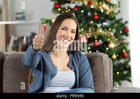 Mujer feliz en navidad con pulgares arriba sentados en un sofá en el salón en casa Foto de stock