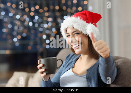 Feliz mujer con pulgares hacia arriba en la navidad sentados en un sofá en el salón en casa Foto de stock
