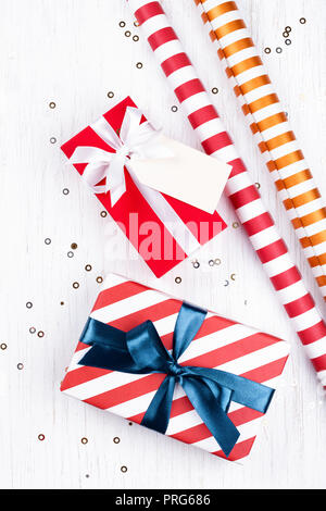Regalos de Navidad envueltos en papel a rayas rojas y atado con cinta azul y blanco, y la etiqueta sobre fondo blanco de madera decorada con destellos. Sentar plana