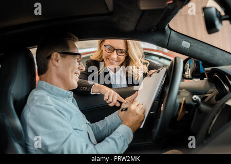 Hombre adulto hembra firma contrato con el concesionario de coches mientras estaba sentado en el coche Foto de stock