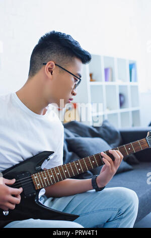Apuesto hombre asiático tocando la guitarra eléctrica en casa