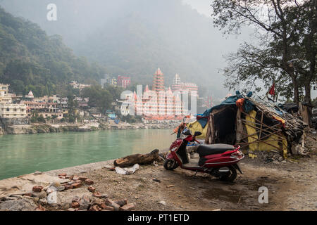 Beggar's hut por el río Ganges Rishikesh en el fondo de un gran templo de cara al otro lado del río. La desigualdad social. El proble Foto de stock