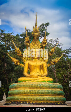 Hermosa estatua de Buda de oro con siete cabezas Phaya Naga bajo las nubes blancas y el cielo azul de fondo. Imagen de Buda sentado de oro al aire libre protegidas por