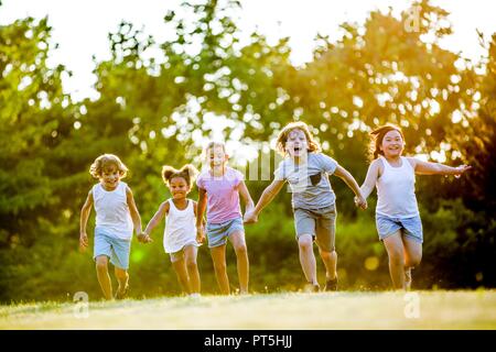 Los niños tomados de las manos y corriendo en el parque, riendo. Foto de stock