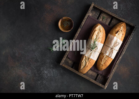 Pan casero fresco con romero y aceite de oliva virgen extra en caja de madera rústica, vista superior, copia el espacio. Sourdough mini pan de baguette.