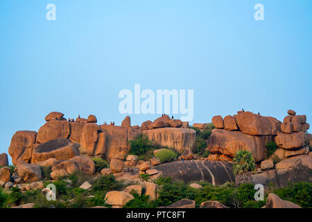 Los turistas occidentales y mochileros socializar y disfrutar de un atardecer desde encima de una gran roca y formación de roca roja en Hampi, India. Foto de stock