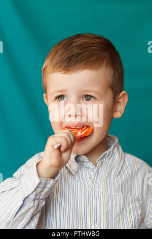 Niño lindo comiendo un lollipop sobre fondo verde. Niño boy comiendo piruleta aislado Foto de stock