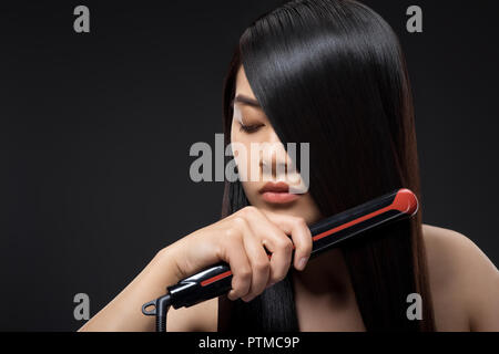 Retrato de joven mujer asiática el cabello liso con alisadores para el cabello aislado en negro Foto de stock