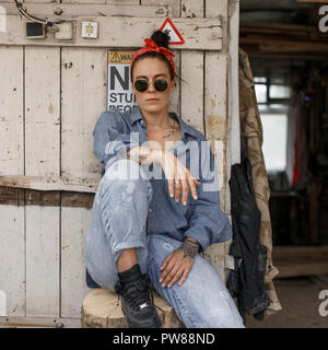 Estilo Mujer con gafas de sol de moda en una moda denim camisa y pantalones vaqueros sentados cerca una pared de madera vintage de stock - Alamy