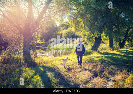 Un hombre con un perro Labrador retriever caminando cerca del lago en el parque