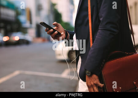 Captura recortada del empresario caminando en el exterior a través de teléfono móvil. El hombre en traje con bolso caminando por las calles de la ciudad con el teléfono celular en la mano.