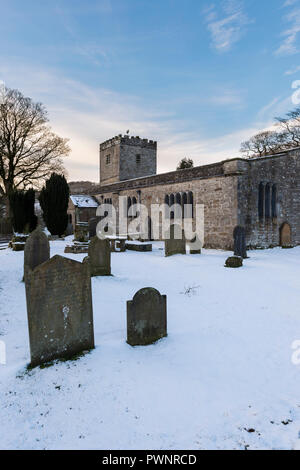 Invierno con nieve exterior de San Miguel y todos los Ángeles Iglesia con lápidas en el cementerio cubierto de nieve - Hubberholme, Valles de Yorkshire, Inglaterra, Reino Unido.