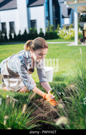 Sonriente rubio mujer disfrutando del proceso de colocación de las plantas en el suelo Foto de stock