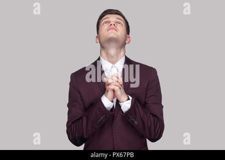 Oh Dios, por favor ayúdame. Retrato de preocuparse guapo joven en traje violeta y camisa blanca, de pie, mirando a la cámara con las palmas de las manos y la oración. Foto de stock