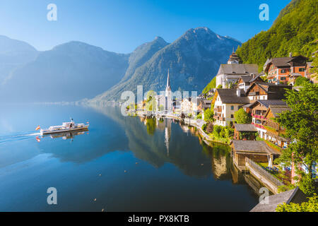 Ver postal clásica de la famosa ciudad lacustre de Hallstatt con barco tradicional en la hermosa la luz de la mañana al amanecer en verano, Salzkammergut, Austria