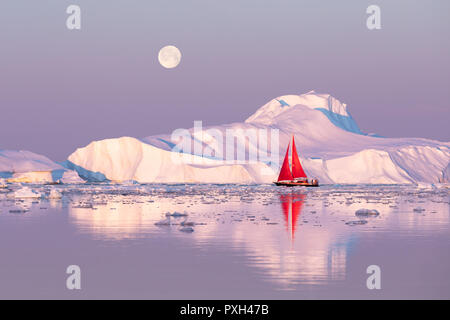 Rojo poco velero navegando entre témpanos flotantes en la bahía Disko glaciar sol de medianoche durante la temporada de verano polar. Ilulissat, Groenlandia. Foto de stock