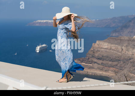 Mujer joven en un vestido blanco y azul disfruta de una caminata alrededor de Santorini Foto de stock