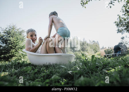 Hermano y hermana jugando con poca agua en la bañera en el jardín