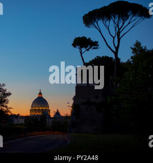 La cúpula de la Basílica de San Pedro en Roma al atardecer, con las antiguas murallas aurelianas que rodean la ciudad y pinos paraguas siluetas contra el cielo. Foto de stock