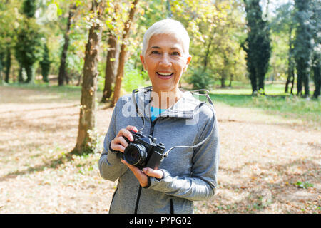 Retrato de encantadora mujer Senior con retro-cámara lista para tomar fotografías en el bosque.