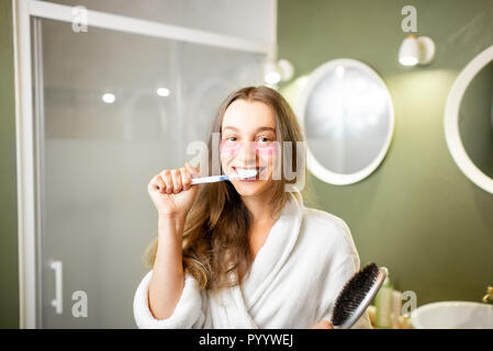 Joven y bella mujer en albornoz cepillando sus dientes en el cuarto de baño Foto de stock