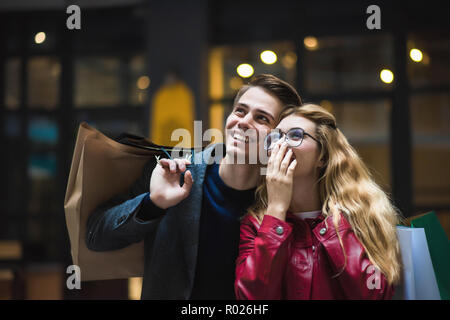 Hermosa pareja con bolsas de compras está hablando y sonriendo mientras hacía compras en el centro comercial se centran en la mujer sorprendida.
