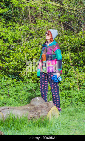 Mujer de pie senior en woodland mirando sonriente, vistiendo elegante vestido multicolor a personas más jóvenes.