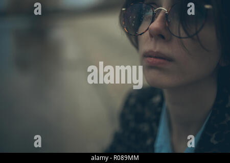 Retrato de mujer con gafas pensativo nublados y gotas de agua sobre ellos durante la lluvia en el atardecer.