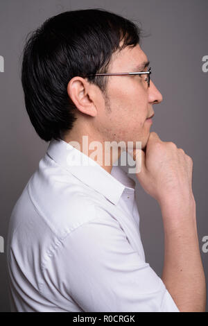 Joven asiático nerd al hombre el uso de anteojos contra el fondo gris Foto de stock