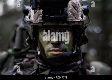 Soldado de las fuerzas especiales con uniforme de combate de camuflaje,  portador de carga, casco, gafas de visión nocturna equipadas, auriculares  de radio tácticos, rifle de asalto con mira de colimador en