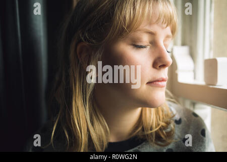 Mujer con los ojos cerrados sentado en la ventana Foto de stock