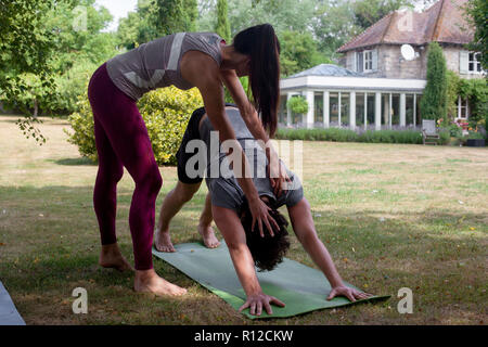 Hembra joven maestro de yoga yoga en jardín, perro boca abajo plantean