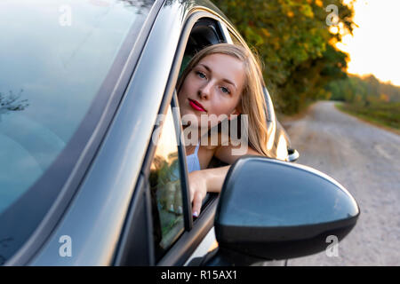 Una joven y bella mujer con cabello largo se sienta al volante del coche y mira por la ventana.