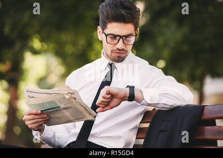 Acuoso Solenoide prima Foto de hombre barbado en traje seria la lectura de periódicos en un banco  en el parque verde y mirando al reloj de pulsera Fotografía de stock - Alamy