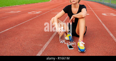 Mujer runner en ropa deportiva sentado en la pista de atletismo