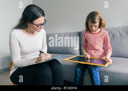 Profesional psicólogo infantil hablando con niño niña en el cargo, el niño dibuja un dibujo. Foto de stock