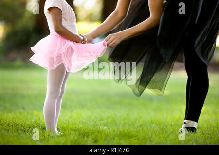 Mitad mujer adulta y su joven hija bailar ballet en un parque.