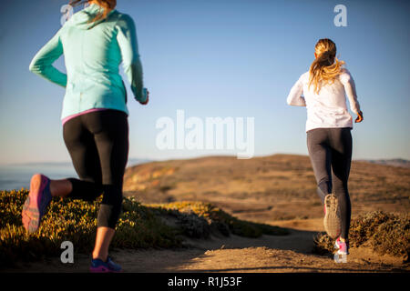 Dos jóvenes mujeres ir de un amanecer jog junto junto a los acantilados por el océano. Foto de stock