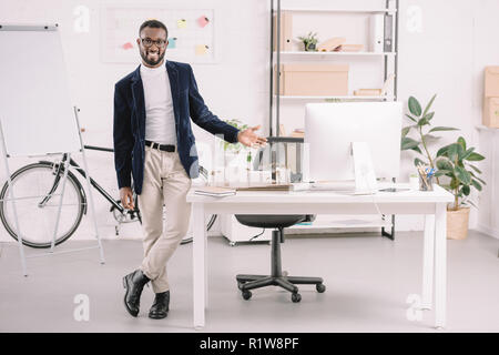 El arquitecto americano africano sonriente trabaja con modelo de edificios comerciales en la oficina con ordenador