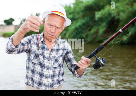 Anciano de pie en Riverside y pruebas sobre la pesca de cebo hook line Foto de stock